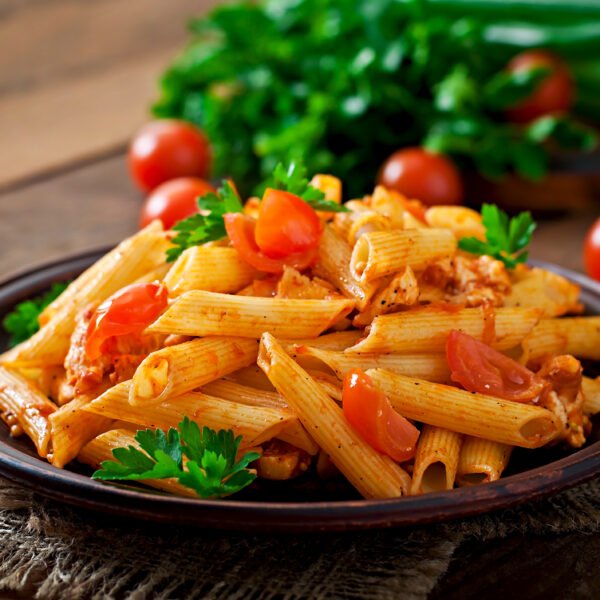 Penne pasta in tomato sauce with chicken and tomatoes  on a wooden table